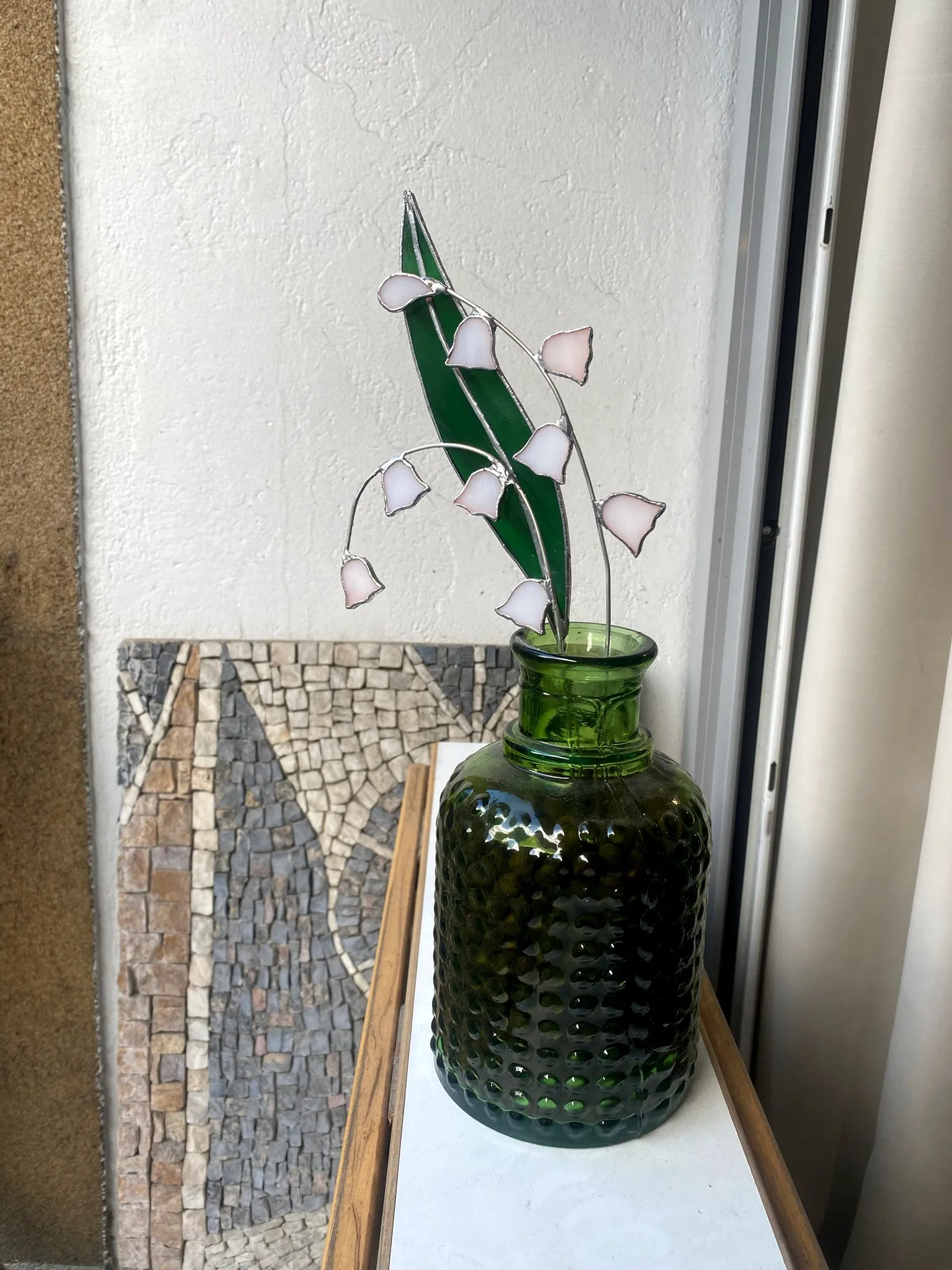 Un brin de muguet en vitrail, clochettes roses et feuilles vertes, dans un vase vert