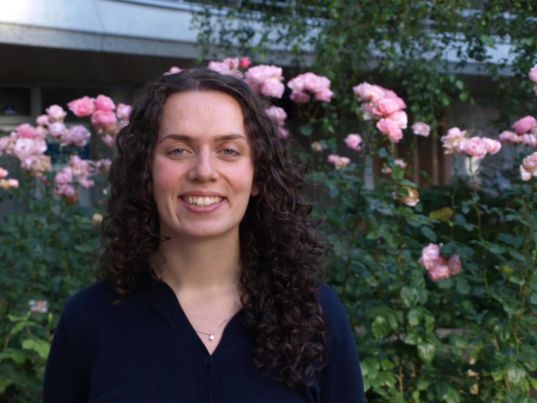 Noa Perez, souriante devant un rosier en fleurs